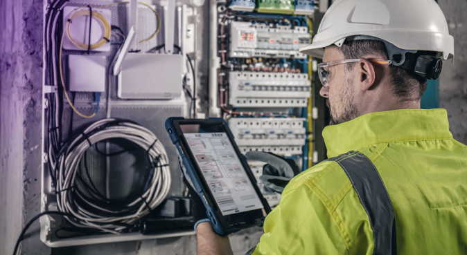 Electrician holding tablet next to electrical boards